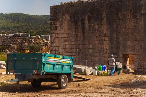A man is pushing a wheelbarrow while standing next to a blue trailer Stock Photos