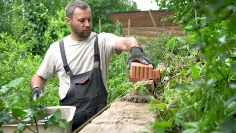 A man is put up a brick wall in the garden. Arrangement of a retaining wall. Stock Footage 202484000