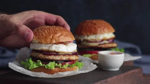 Man put bun on burger with chicken cutlet fries egg vegetables Stock Footage 122801576