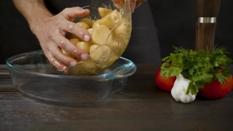 Man put potatoes from the bowl to the baking dish in the dark kitchen Stock Footage 112739727