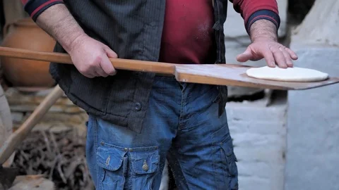 The man put the raw flatbread on a wooden spatula and put it in the oven. Stock Footage 125523677