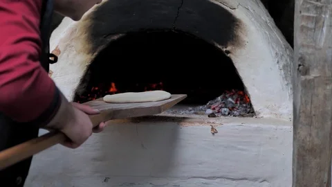 The man put the raw flatbread on a wooden spatula and put it in the oven. Video stock 125523683