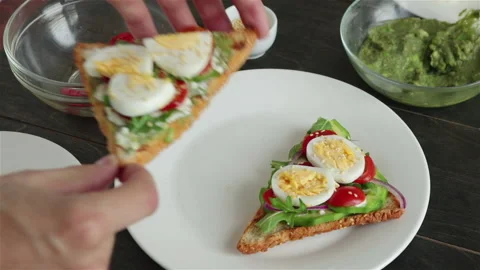 Man put sandwich with avocado boiling egg cherry tomatoes arugula on the plate Stock Footage 102883377