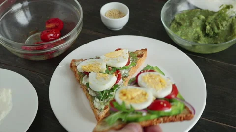 Man put sandwich with avocado boiling egg cherry tomatoes arugula on white plate Stock Footage 132331389