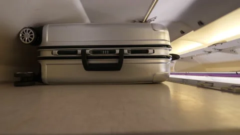 Man put small rollaboard suitcase at overhead shelf and close locker door Stock-Footage 131887458