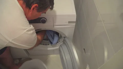 Man put washed laundry into dryer Stock Footage 144963133