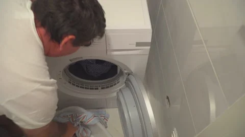 Man put washed laundry into dryer Stock Footage 144963934