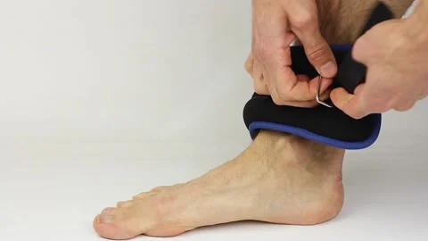 Man puts on ankle weights on bare leg on white background, home sport Video stock 156474653