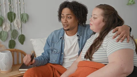 Man puts arm around plus size woman on bed holding remote control and watch.. Stock Footage 337389343