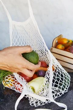 Man puts avocado to the eco string bag with fresh vegetables - tomatoes, purple Foto stock