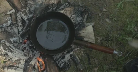 Man puts bacon into frying pan on campfire Video stock 76703436