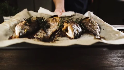 Man puts a baking sheet with fresh baked fish on the table. Stock Footage 125581188
