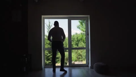 Man puts on a belt in the backlight. A man is standing near the window Stock Footage 204925533