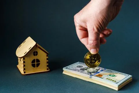 A man puts a bitcoin coin on a stack of one hundred dollar bills in front of Stock Photos