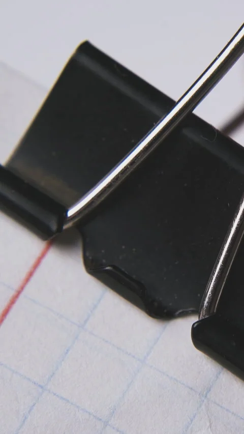 Man puts black clamp on checkered paper sheets macro Stock Footage 317387086