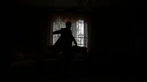 Man puts on black jacket standing before window Stock Footage 95830161