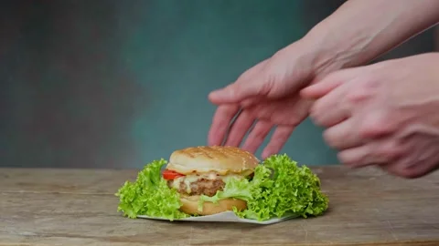 Man Puts Cheeseburger on table on green background. Close up Stock Footage 234899739