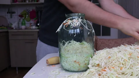 A man puts chopped cabbage and carrots with dill seeds in a jar. Compacts it  Stock Footage 220713291