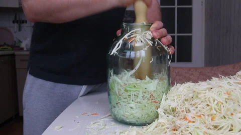 A man puts chopped cabbage and carrots with dill seeds in a jar. Compacts it  Stock Footage 220713328