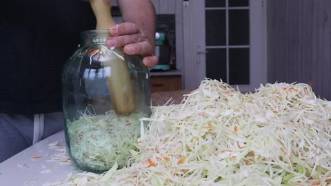 A man puts chopped cabbage and carrots with dill seeds in a jar. Compacts it  Stock Footage 220713344