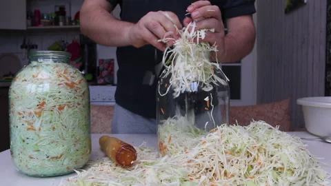 A man puts chopped cabbage and carrots with dill seeds in a jar. Compacts the Stock Footage 220713401