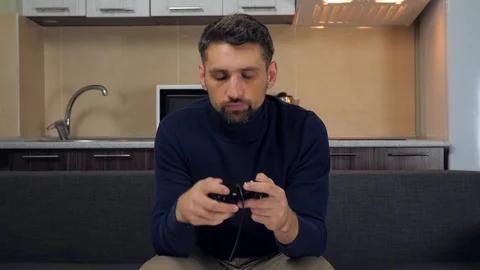 Man is puts down a gamepad, rises from the couch and leaves Stock Footage 121842036