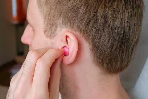 A man puts a earplug in his ear. Wax pink ear plug Stock Photos