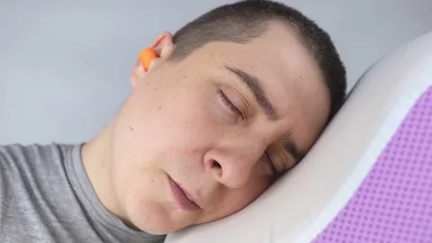 The man puts on earplugs. Close-up of an orange noise barrier. Deep sleep. The E Stock Footage 187969013