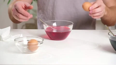 A man puts an egg on a spoon into a glass cup with a dye. Dyeing eggs with Stock Footage 236920963