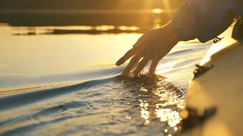 Man puts fingers down lake kayaking against backdrop of golden sunset, unity Stock Footage