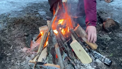 A man puts firewood and logs on a small fire. Yellow-orange flames Stock-Footage 179345965