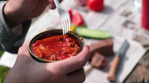 A man puts a fork in a jar of canned fish in tomato sauce. Outdoor picnic. Stock Footage 163713164