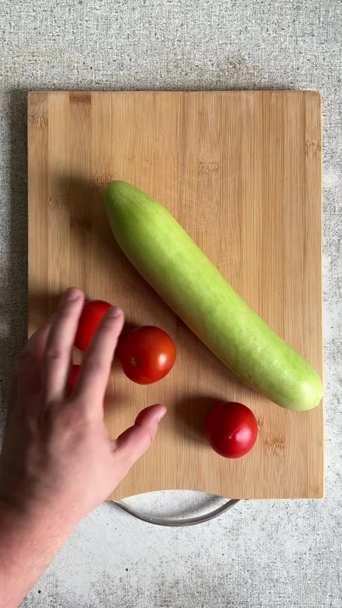 Man puts fresh raw green juicy cucumber and red tasty tomato on wooden board Stock Footage 280880333