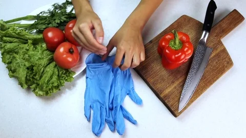Man puts on gloves on arms by table where vegetables lie in kitchen. Stock Footage 82159958