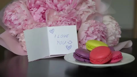 A man puts a greeting card on the table next to a bouquet of peonies Stock Footage 195879530