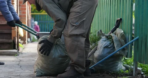 A man puts a heavy bag of garbage on a wheelbarrow held by a woman. Video stock 161073323