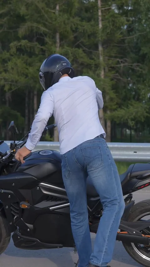 A man puts on a helmet, gets on an electric motorcycle and rides off. Vertical Видео 265206757