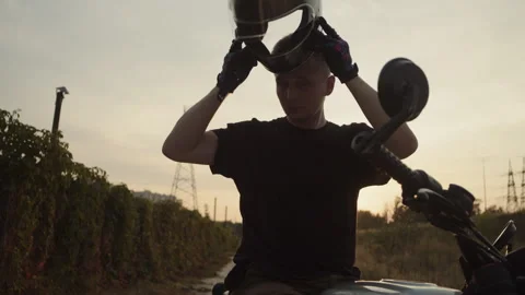 A man puts on a helmet while sitting on a motorcycle during sunset Video stock 253446809
