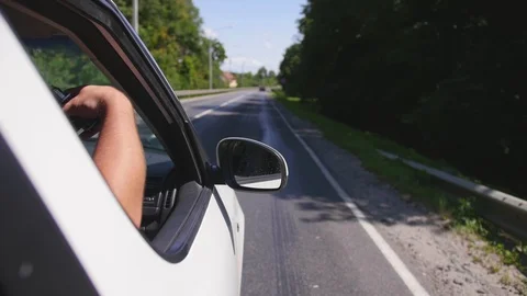 Man puts his hand out car window and vaping an electronic cigarette on a sunny Stock Footage 114979934