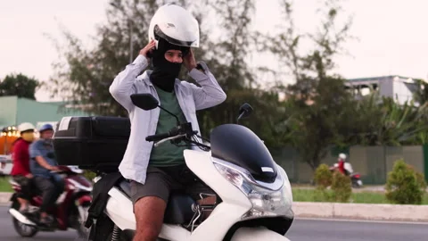 The man puts on his helmet while sitting on the moped. Video stock 312798901