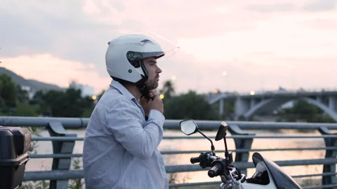 A man puts on his motorcycle helmet against a pink sunset. Stock Footage 312794842