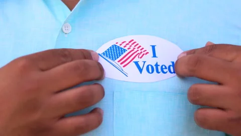 Man puts I Voted sticker with American Flag on the shirt. Stock Footage 141833094