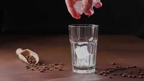 Man Puts Ice Cubes in a empty tall Glass on a black background Stock Footage 238086352
