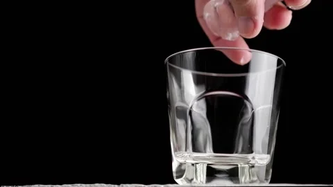 A man puts ice cubes in a whiskey glass. Preparation of an alcoholic cocktail. Stock Footage 167798502