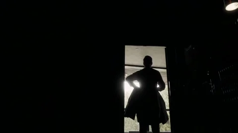  man puts on a jacket in the backlight. A man is standing near the window and ge Stock Footage 133871366