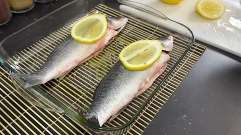 Man puts lemon slice on fresh sea bass. Preparing the fish for baking. Vidéo 237840627