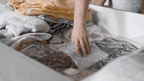 Man puts linens into under the bed storage. Bedroom organization. Small space co Stock Footage 305313999