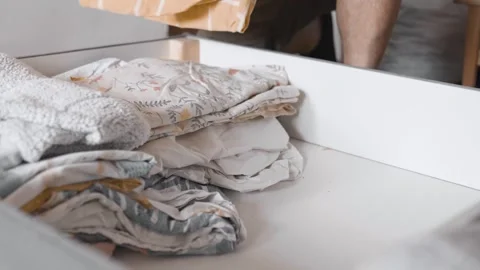 Man puts linens into under the bed storage. Bedroom organization. Small space co Stock Footage 305314306