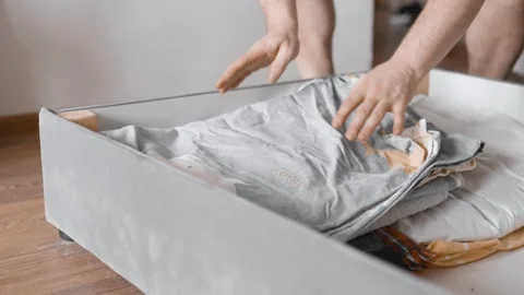  Man puts linens into under the bed storage. Bedroom organization. Small space c Stock Footage 305314876