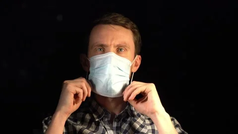 A man puts on a mask against a dark background 库存影片 142907255